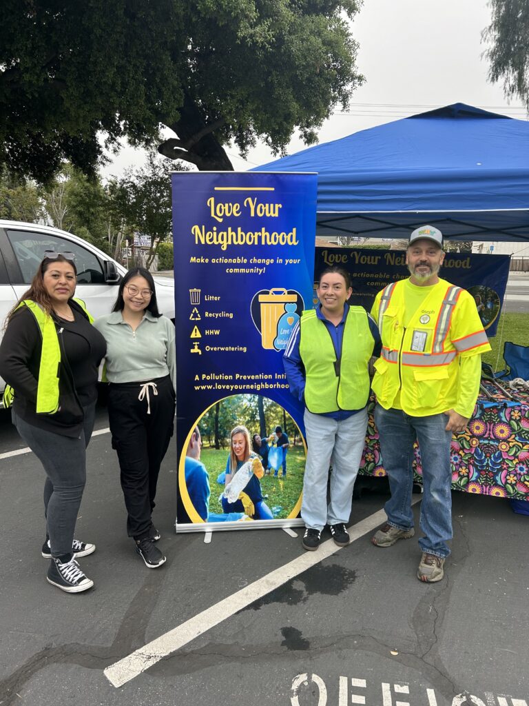 "Love your Neighbor make actionable change in your community "poster with volunteers in safety vests at a booth at a community event in a Wildomar parking lot.
